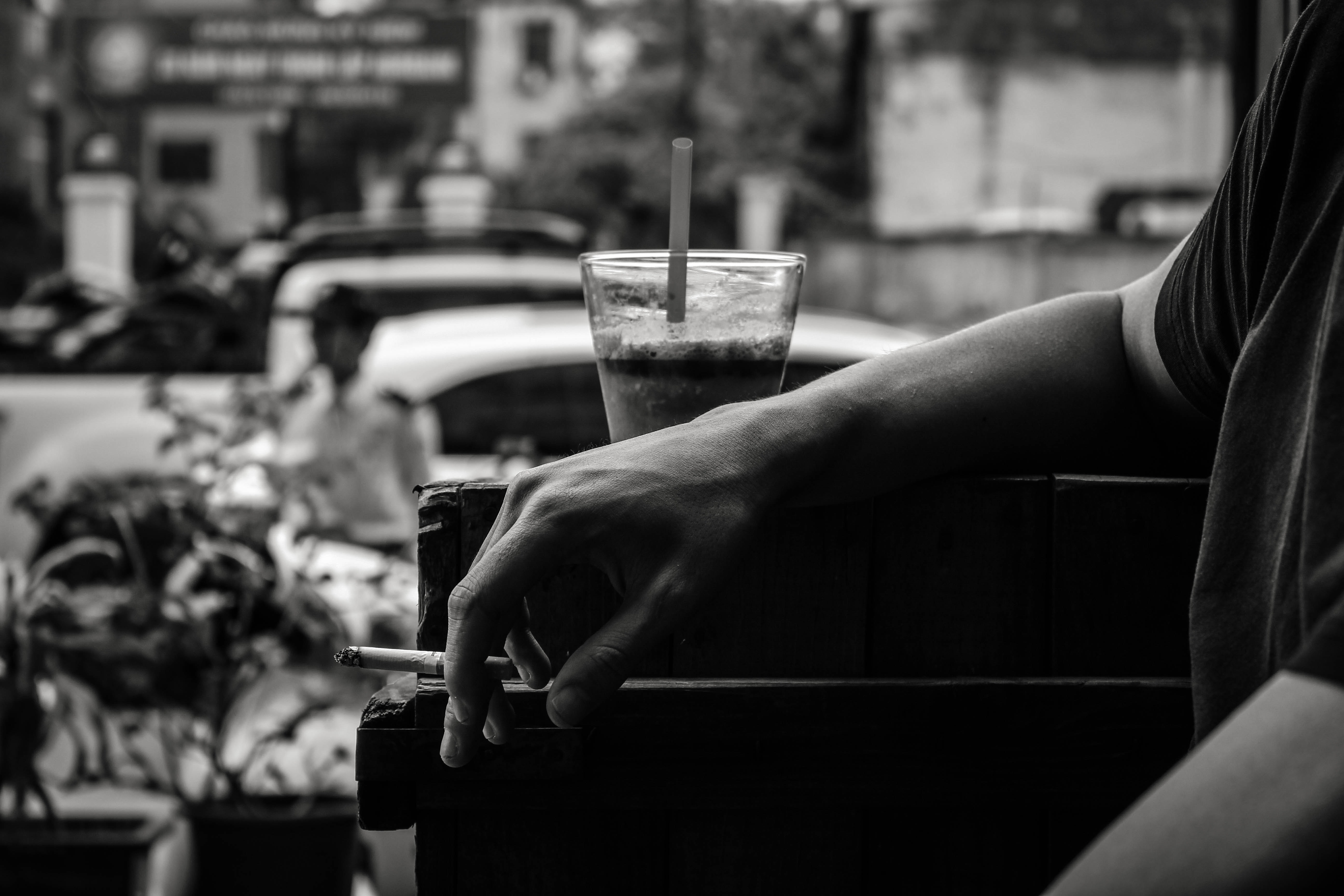 black and white photo of hand holding cigarette next to drink with straw