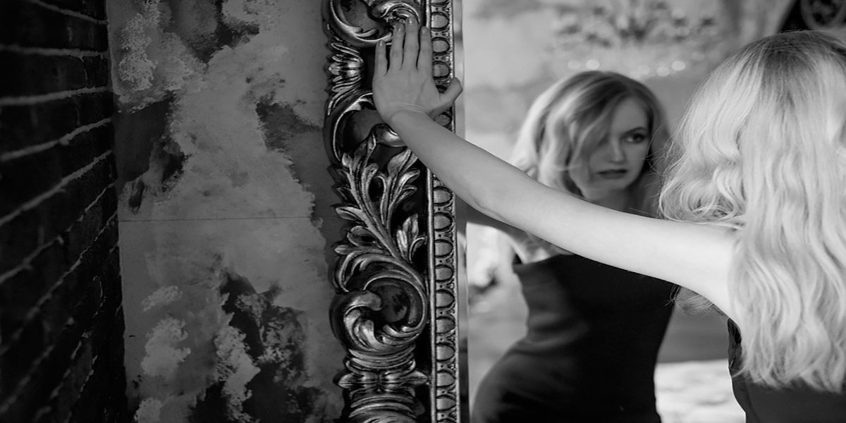 black and white photo of woman standing in front of ornate mirror